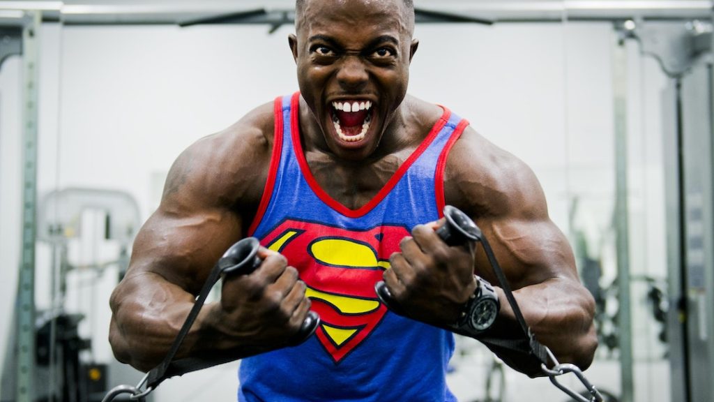 Man doing intense workout with weights wearing a Superman shirt.